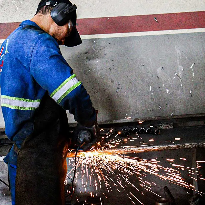 Homem com uniforme azul cortando cilindros de aço
